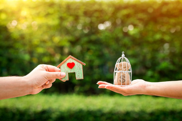 Loan or save for buy a house and real estate concept, Man and woman hand holding money bags and a home model with red heart put together in the public park.