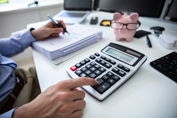 Businessman Calculating Invoice With Piggy Bank