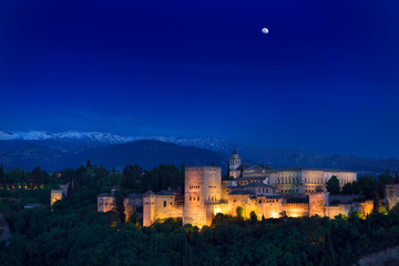 Moonrise over hilltop Alhambra Palace fortress complex at twilight Granada with Sierra Nevada...