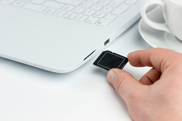 insert sd card in laptop, hand with sd card next to a sd card slot in a laptop