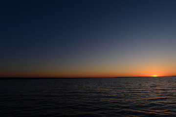 Sunset in the blue sky on the horizon above the water of the lake
