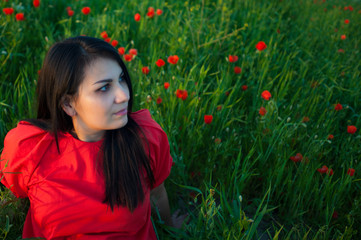 Naklejka premium Beautiful girl in red shirt has a relax in the field of red poppy flowers. Young woman enjoys of beauty nature.