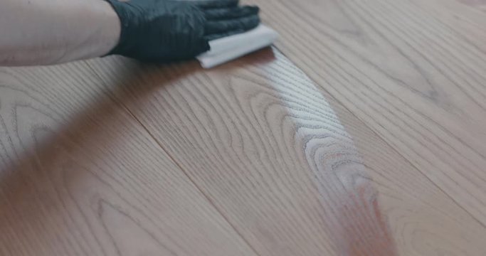 Closeup man in gloves cleaning ash wood floor with wet cloth