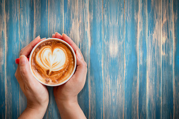 Top view of woman hand holding a red cup of coffee with latte art on the vintage blue background, Happiness and refreshing in time concept.