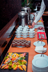 Coffee break served on the table – pieces of chocolate cake on black stone tray, fruits and tea-cups, plates. Selective focus.