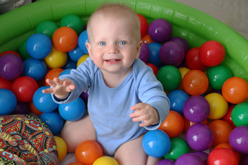 Fototapeta na wymiar One year old baby boy is playing in ball pool on safety playground. Having fun with toys