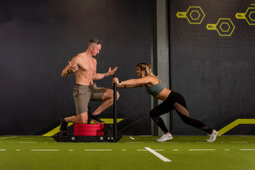 Male and Female workout partners with male standing showing his six pack abs on the weighted sled as his female partner pushes 