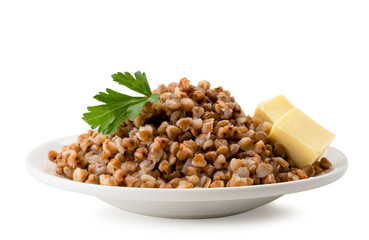 Boiled buckwheat in a plate with parsley leaf and butter cubes on a white. Isolated.