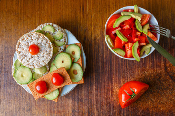Rice and gluten-free bread with avocado and tomatoes. Avocado salad of peppers and tomatoes. Two vegetarian dishes on the table with a knife fork and half a tomato.