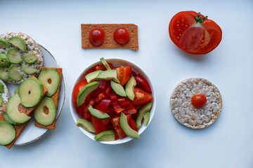a plate with a salad of avocado peppers and tomatoes. vegan gluten-free breads smeared with avocado and tomatoes. Rice toast bread with fresh avocado on the white background