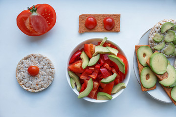 a plate with a salad of avocado peppers and tomatoes. vegan gluten-free breads smeared with avocado and tomatoes. Rice toast bread with fresh avocado on the white background.