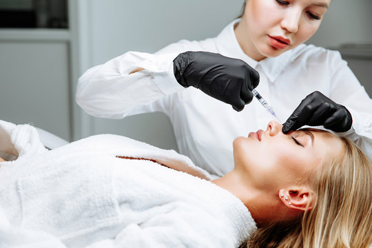 The doctor cosmetologist makes prick in the nose to correct the hump of a beautiful woman in a beauty salon.