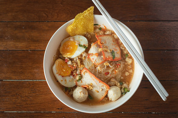 Spicy noodles in a bowl with pork and boiled eggs as ingredients and chopsticks on the table, top view