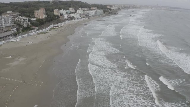 Aerial view of the coast of Anzio, a small sea town near Rome, in Italy. There is no one on the beach on this cold spring day. The blue sea with its waves is rough. In the sky there are some clouds.