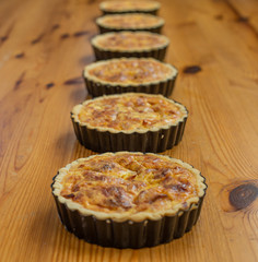 Six Quiche in a line on a pine table