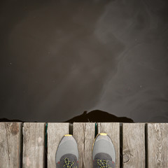 Closeup of the feet on the edge of the pier against the background of water. River, lake or reservoir. Thoughts of suicide or just a walk along the promenade in the open air