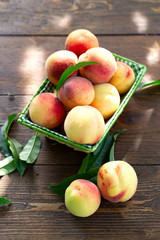 Fresh peaches fruits with leaves in basket on dark wooden rustic background