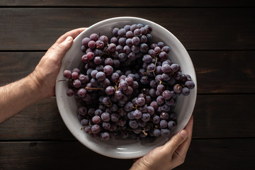 Male hands holding a bowl with red grapes on wooden table
