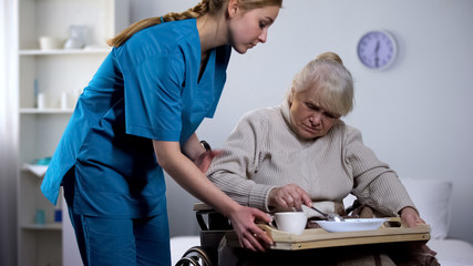 Nurse serving unappetizing diet dinner to old handicapped woman, taking care