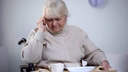 Unhappy old female in wheelchair refusing to eat hospital lunch, feeling lonely
