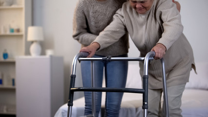 Volunteer helping elderly woman using walking frame, rehabilitation after trauma