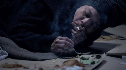 Homeless person smoking cigarette, lying on floor in dirty shelter, addiction
