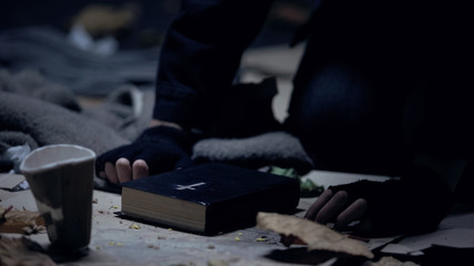 Homeless beggar sitting on floor with bible and praying for help, strong belief - obrazy, fototapety, plakaty