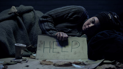 Help word on poster holding poor homeless beggar lying on dirty street, charity