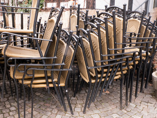 aufeinander gestapelte Stühle stehen am Rande eines Cafes. Es ist schlechtes Wetter und sie werden nicht gebraucht.