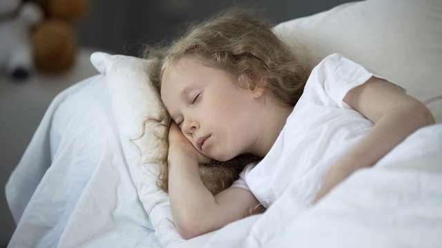 Blond little girl sleeping in comfortable bed at home, calm rest for good health