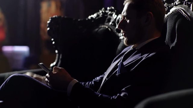 Rich lifestyle, professional success, profit, finance concept. Bearded man with confident face holds dollars. Entrepreneur sits on elegant sofa and counts money. Broker looks rich and successful.