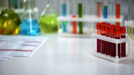 Medical lab worker holding capsule, blood samples on background, pharmaceuticals