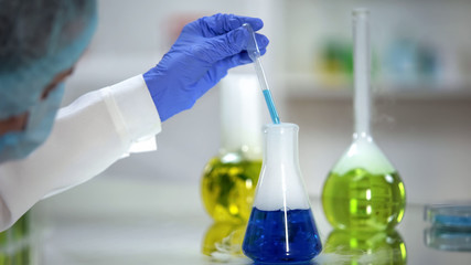 Chemist taking blue substance sample from flask, washing agent analysis, test