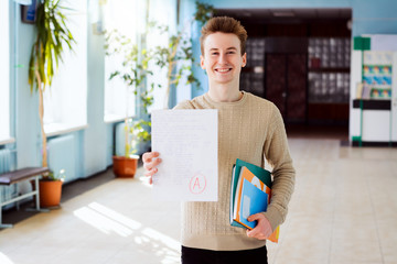 Happy caucasian student holds checked paper with final test with A grade, shows it to the camera and looks very satisfied. Student shows high academic performance and excellent results in studying