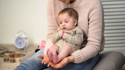 Cute tiny newborn baby sitting barefoot on young lady lap, child skin care