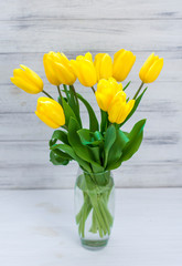 Bouquet of yellow tulips in a vase on a white wooden board background