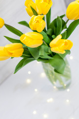 Bouquet of yellow tulips and garlands in a vase on a white wooden board background