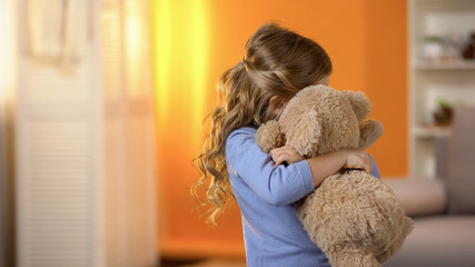 Small girl hugging teddy bear, problems with socialization, lack of friends