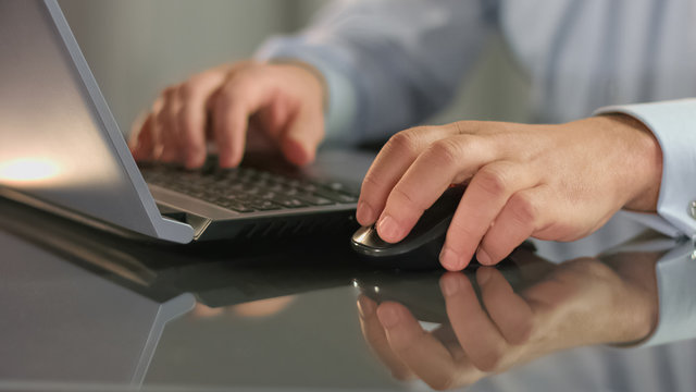 Stock exchange broker working on laptop holding computer mouse, scrolling site
