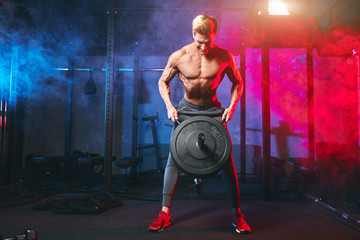 Fototapeta na wymiar Caucasian muscular shirtless bodybuilder, flexing weight plates on iron bar over smoky dual color background. Weightlifting training.