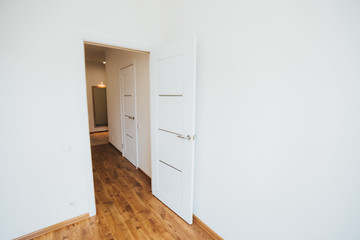 modern light interior. room with white walls and wooden floor. white open door.