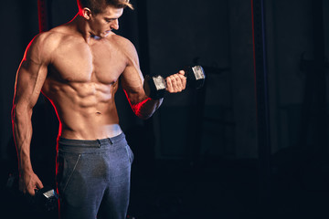 Fototapeta na wymiar Young caucasian male trainer with muscular well-trained torso posing at cross fit studio holding dumbbells in hands