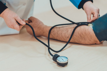A doctor measuring blood pressure of a male patient with sphygmomanometer and stethoscope in the hospital. Health care concept. 