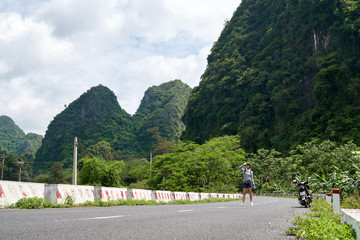 Obraz premium Woman traveler with helmet on her head and motorbike on the road, Cat Ba Island in Vietnam.