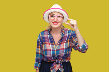 I need a little more. Portrait of pleased modern stylish mature woman in casual style with hat and eyeglasses standing and asking for something more. indoor studio shot isolated on yellow background.