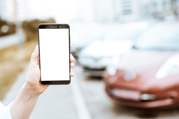 Smartphone in hand with a white screen on the background of cars. Order a taxi from a mobile phone. 