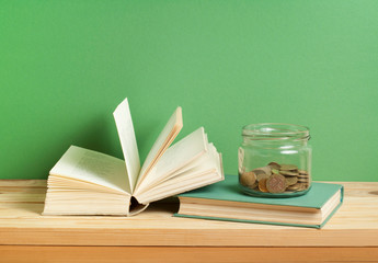 Coins in glass jar and books on wooden table. Saving,financial and education concept.