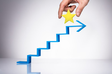 Person's Hand Placing Yellow Star On The Increasing Staircase