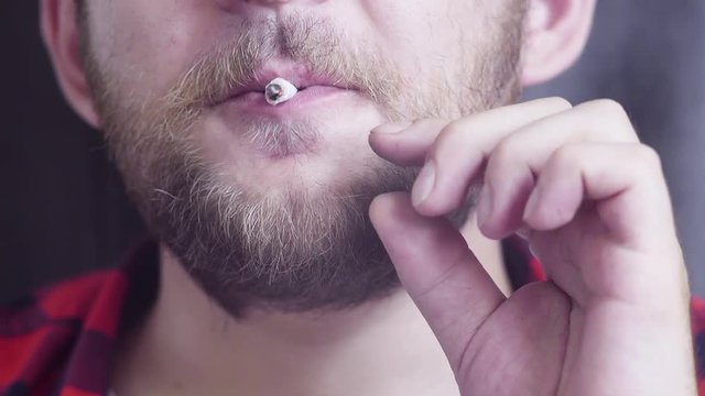 Portrait of face of mature nice-looking caucasian bearded guy slowly smoking rolled cigarette and staring at camera with smile.