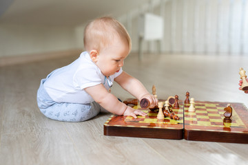 Two babies boy and girl playing chess on the white wooden floor at home